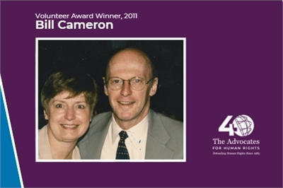 [ai] A man and a woman smiling together in a formal portrait. The man is wearing glasses and a suit, while the woman has short hair and is wearing a light-colored blouse. Background includes a design for an award and text indicating "Volunteer Award Winner, 2011" and the name "Bill Cameron."